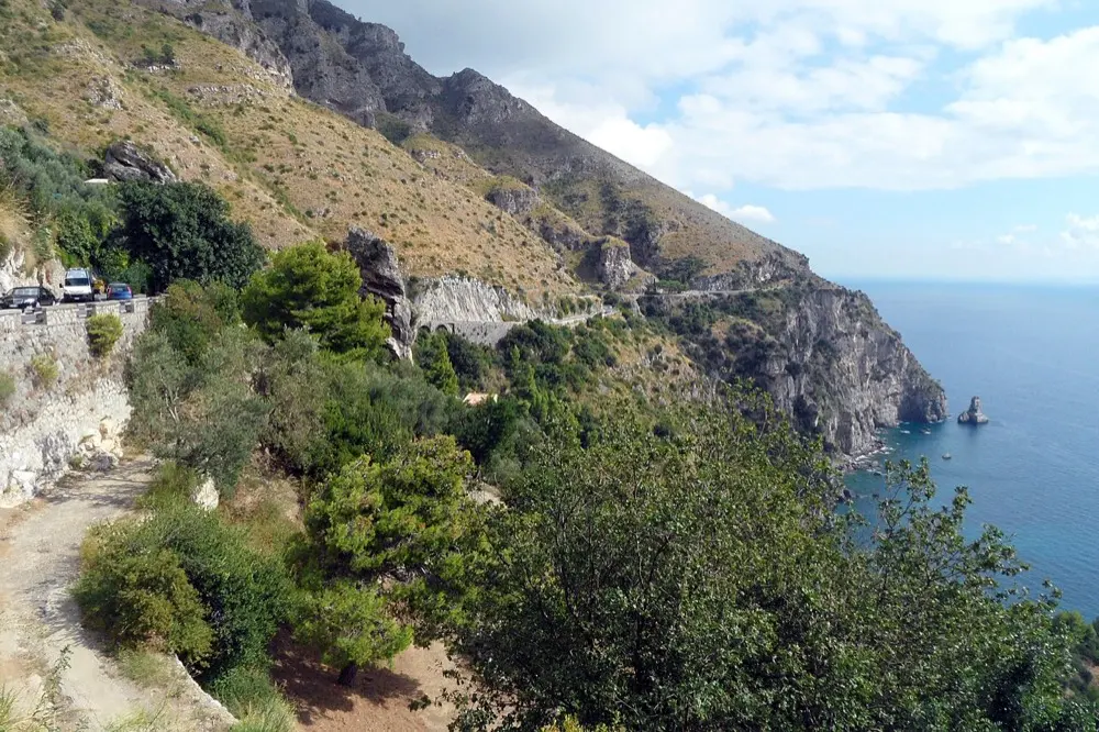 The SS163 Amalfitana cut into the cliffs above the sea, with cars parked along the wall