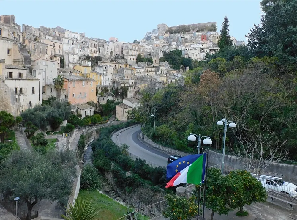 The baroque old town of Ragusa Ibla in Sicily, its houses stacked up the hillside above a curving road